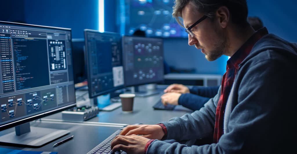 Développeur web concentré codant sur plusieurs écrans dans un bureau moderne high-tech à l'ambiance bleue.